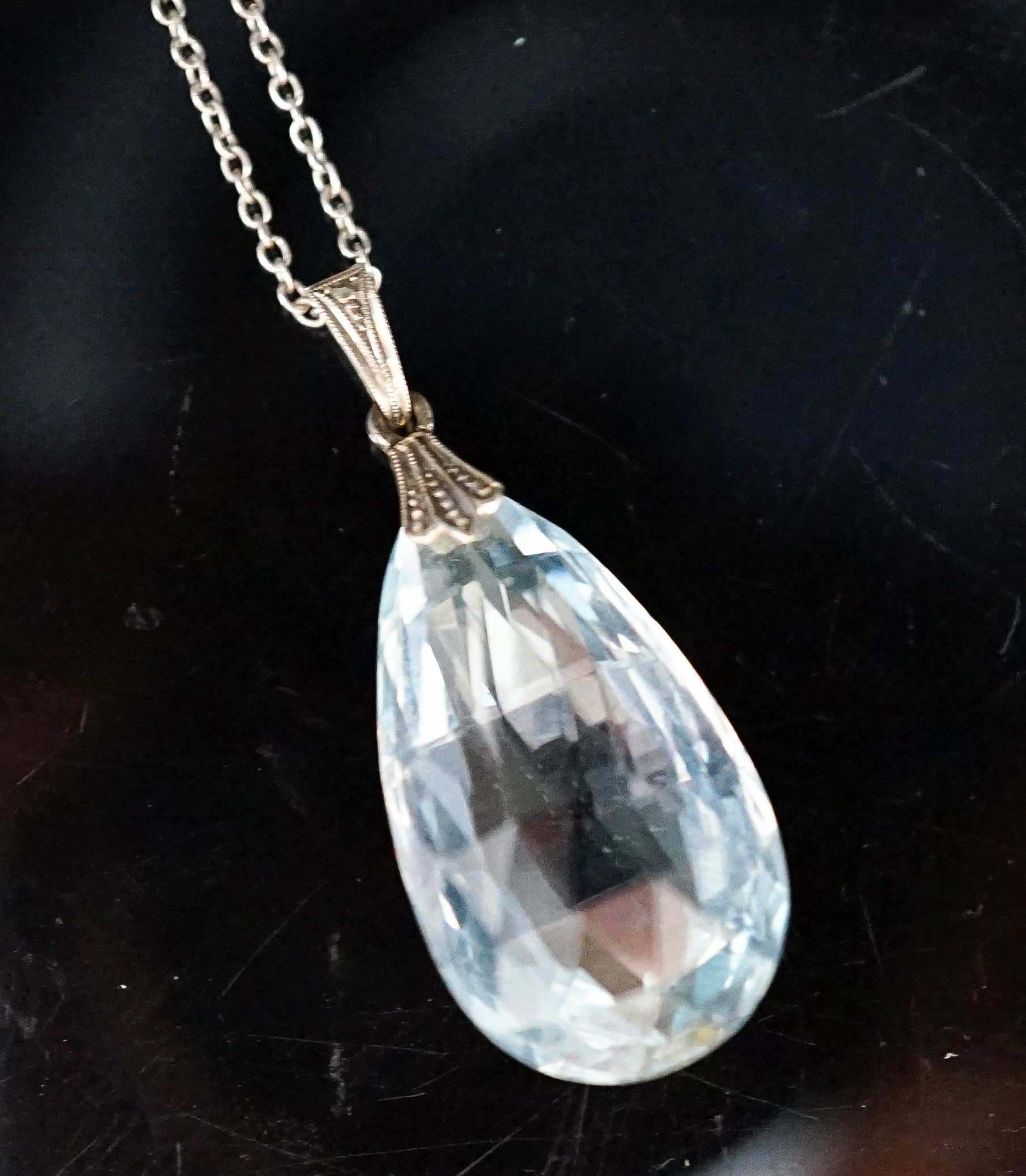 An 18ct mounted facetted pear cut aquamarine set pendant, 33mm, on a 375 white metal fine link chain, 45cm, gross weight 5.2 grams.